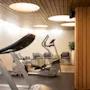 Ett modernt gym med träningsmaskiner och en bekväm sittgrupp, med varm belysning och trädetaljer.