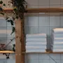Fresh white towels on wooden shelves, adorned with lush green plants, set against a clean tiled background.