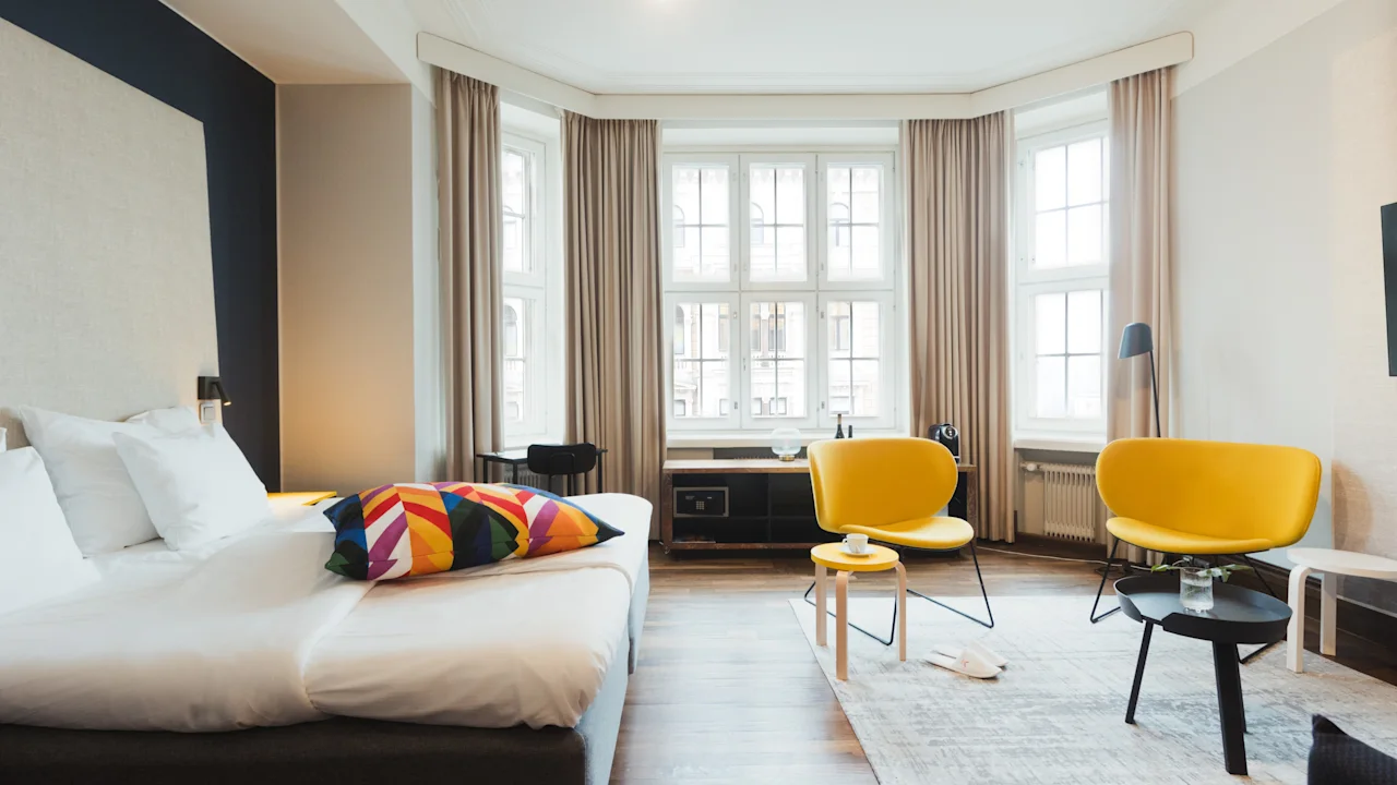 Valoisa hotellihuone, jossa on mukava sänky, kaksi keltaista tuolia ja suuret ikkunat, luo kutsuvan ja rentouttavan tunnelman.