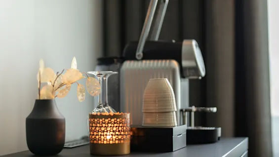 Et koselig hjørne med en kaffemaskin, dekorativ vase og et varmt glødende lys, som skaper en innbydende atmosfære.