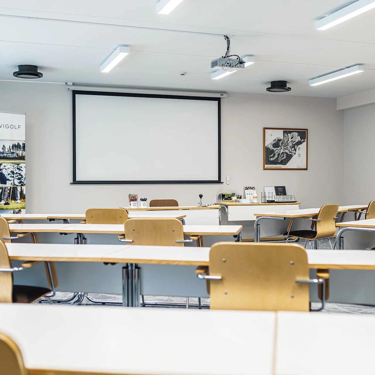 Conference room features rows of wooden chairs facing a blank projector screen, with banners and framed pictures on the walls. Text: "WYGØLF."