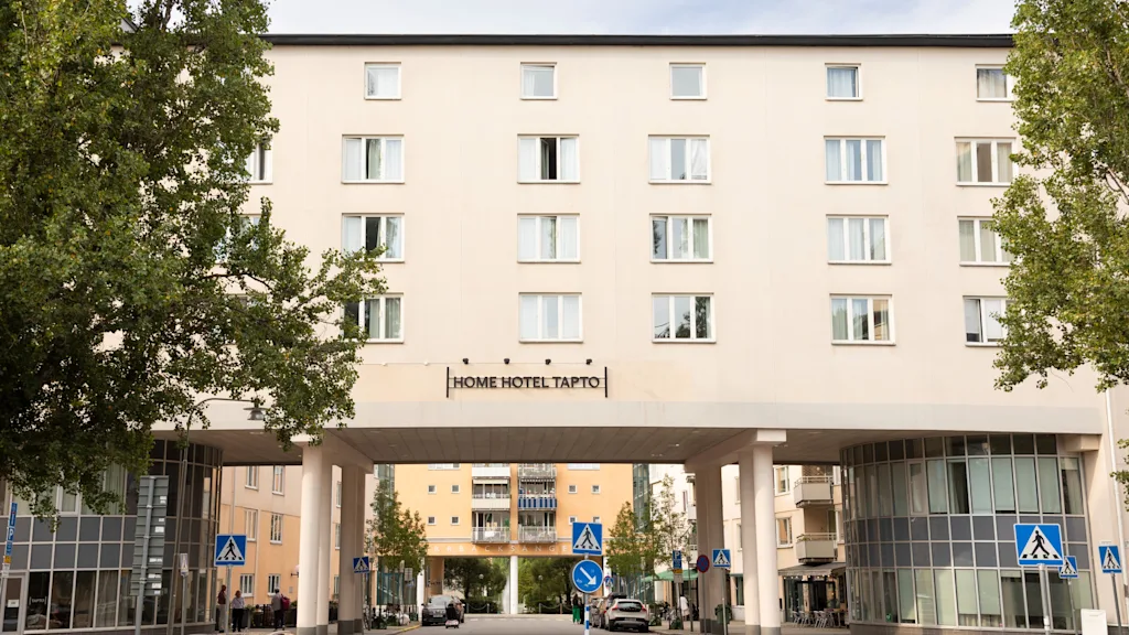 Exteriör vy av Home Hotel Tapto i Stockholm, en stor byggnad som sträcker sig över en gata med bilar och träd.