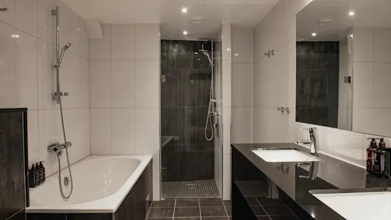 Ett modernt hotellbadrum designat för komfort, med ett avkopplande badkar, en duschkabin och ett dubbelt handfat.