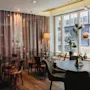 A cozy dining area at Home Hotel Uppsala with dark tables, comfortable chairs, and large windows showing ON and a city street.
