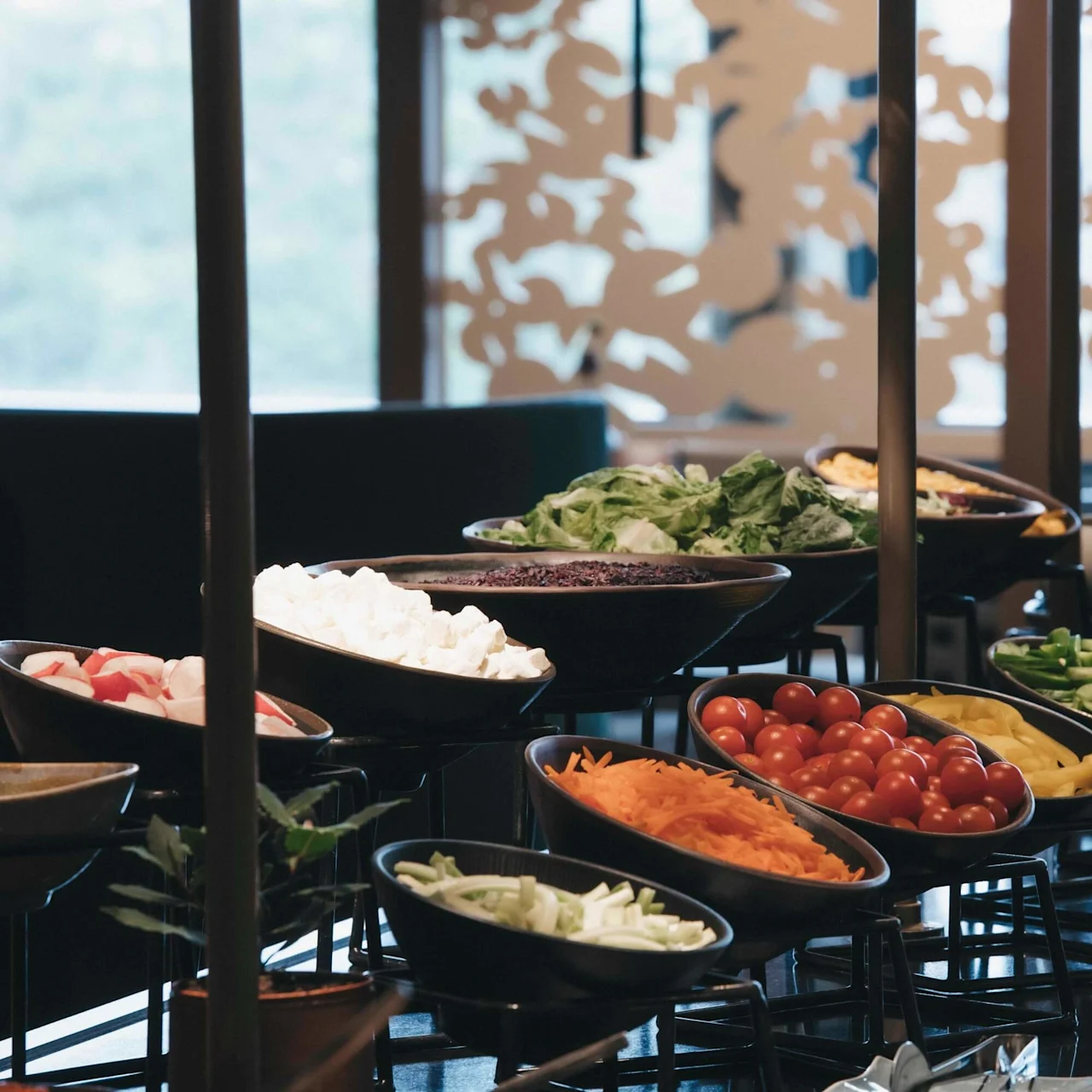 En variert salatbar med friske grønnsaker og tilbehør i skåler, plassert i et moderne spiseområde.