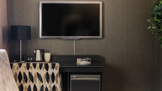 En bekväm hotellrumsinredning med en väggmonterad TV, en förfriskningsstation och en mysig sittplats.
