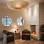 A cozy hotel lobby seating area with two leather armchairs, a glowing fireplace, and round windows looking out to trees.