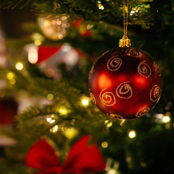 Nærbilde av en rød julekule med gullspiraler på et belyst juletre.
