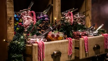 En festlig godisbar med burkar fyllda med färgglada sötsaker, dekorerad med grönska, kottar och ljusslingor, samt polkagrisar.