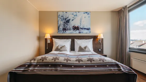 Mysigt hotellrum med en bäddad dubbelsäng, mönstrat överkast och en vintertavla på väggen.
