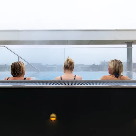 Tre personer kopplar av i det varma vattnet på Quality Hotel Öresund – Rooftop Spa och njuter av utsikten.