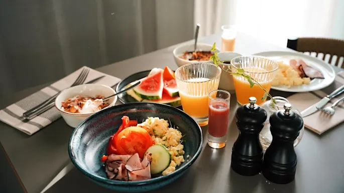 A variety of breakfast items arranged on a table, suggesting a meal in progress inside a room with natural lighting.