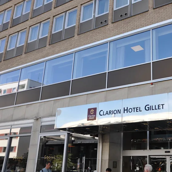 English: Facade of Clarion Hotel Gillet with reflective metal canopy above entrance; people stand nearby. Upper building features rows of windows.