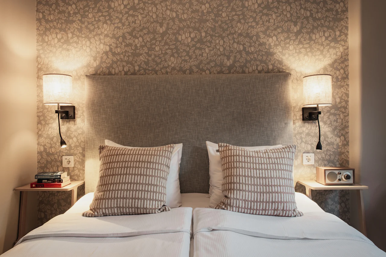 Et hyggeligt soveværelse på Home Hotel Wellington med to senge, sengelamper og mønstret tapet, der indbyder til et afslappende ophold.