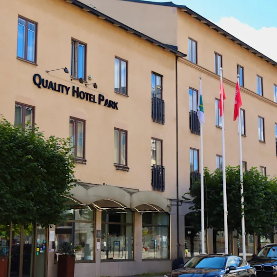 Exteriör vy av Quality Hotel Park Södertälje med bilar parkerade på gatan och flaggor som vajar framför byggnaden.