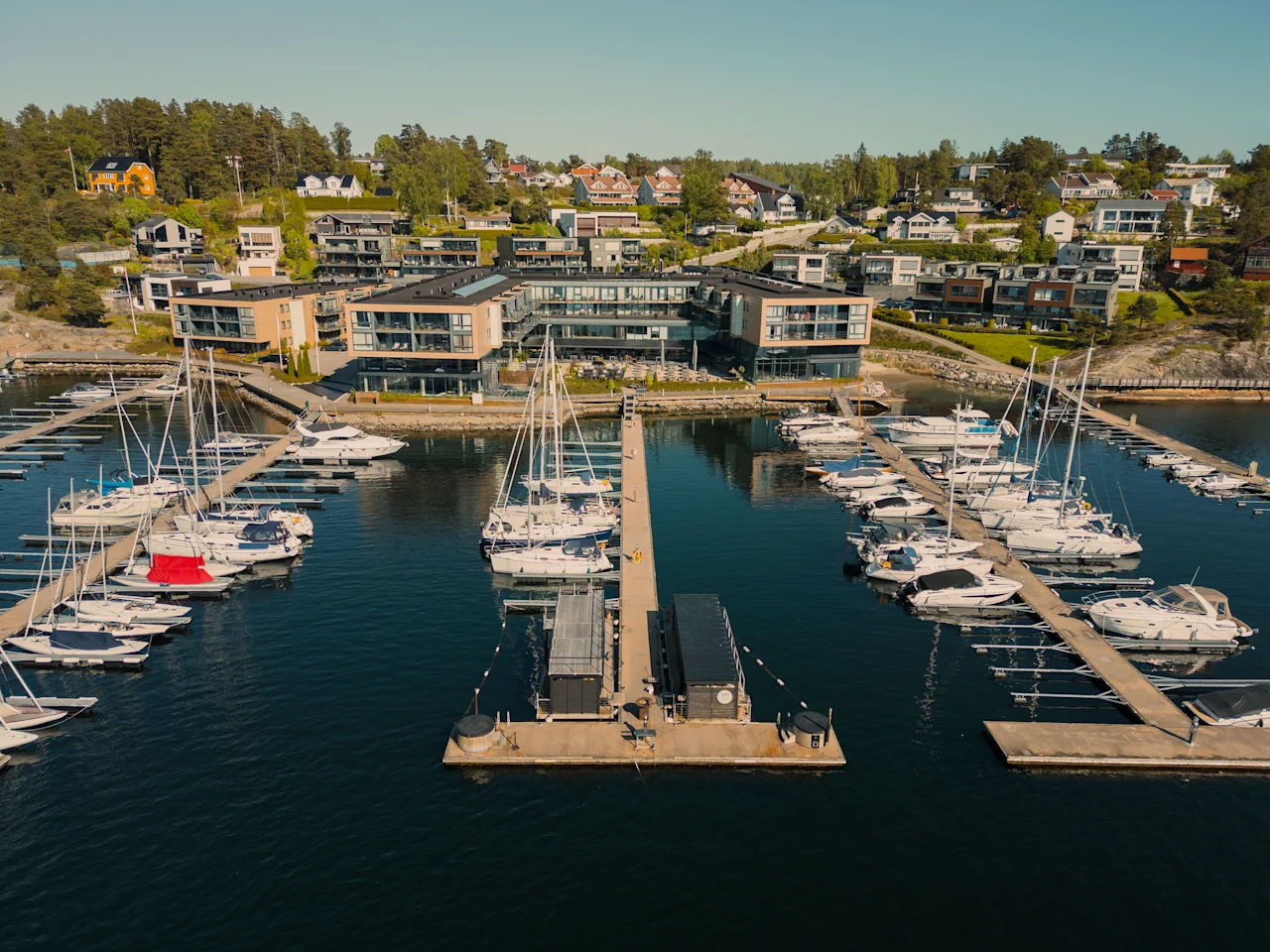En luftfoto af en livlig marina med mange både fortøjet, mod en baggrund af moderne bygninger og huse på en bjergskråning.