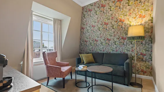 Et innbydende hotellrom på Home Hotel Gabelshus med en komfortabel sofa, en lenestol og en levende blomstret tapet.