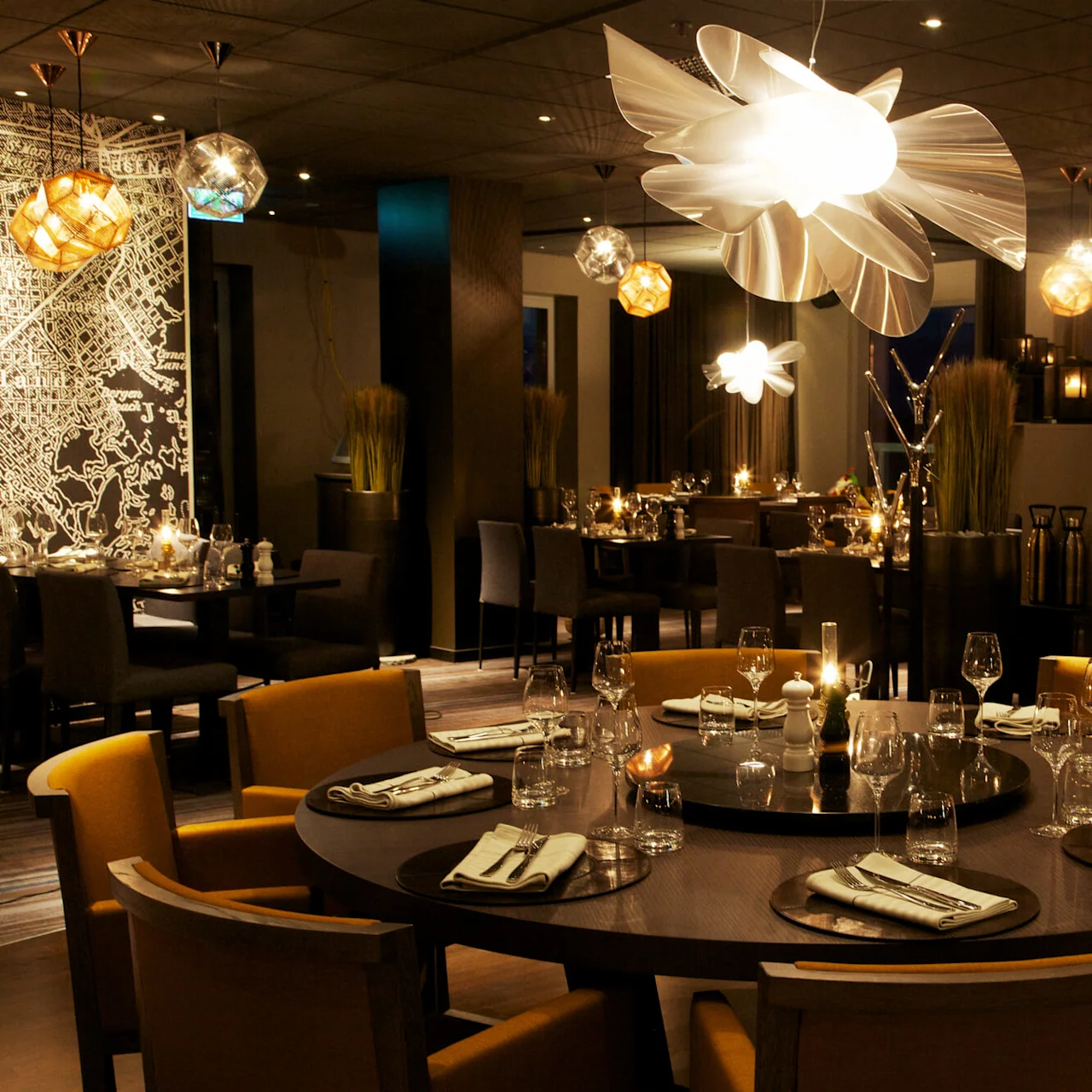 Elegant matbord dukat med glas och vikta servetter i en svagt upplyst restaurang omgiven av modern inredning och konstnärliga belysningsarmaturer.