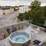 Rooftop terrace with a bubbling hot tub and comfortable seating, overlooking a city street and buildings.