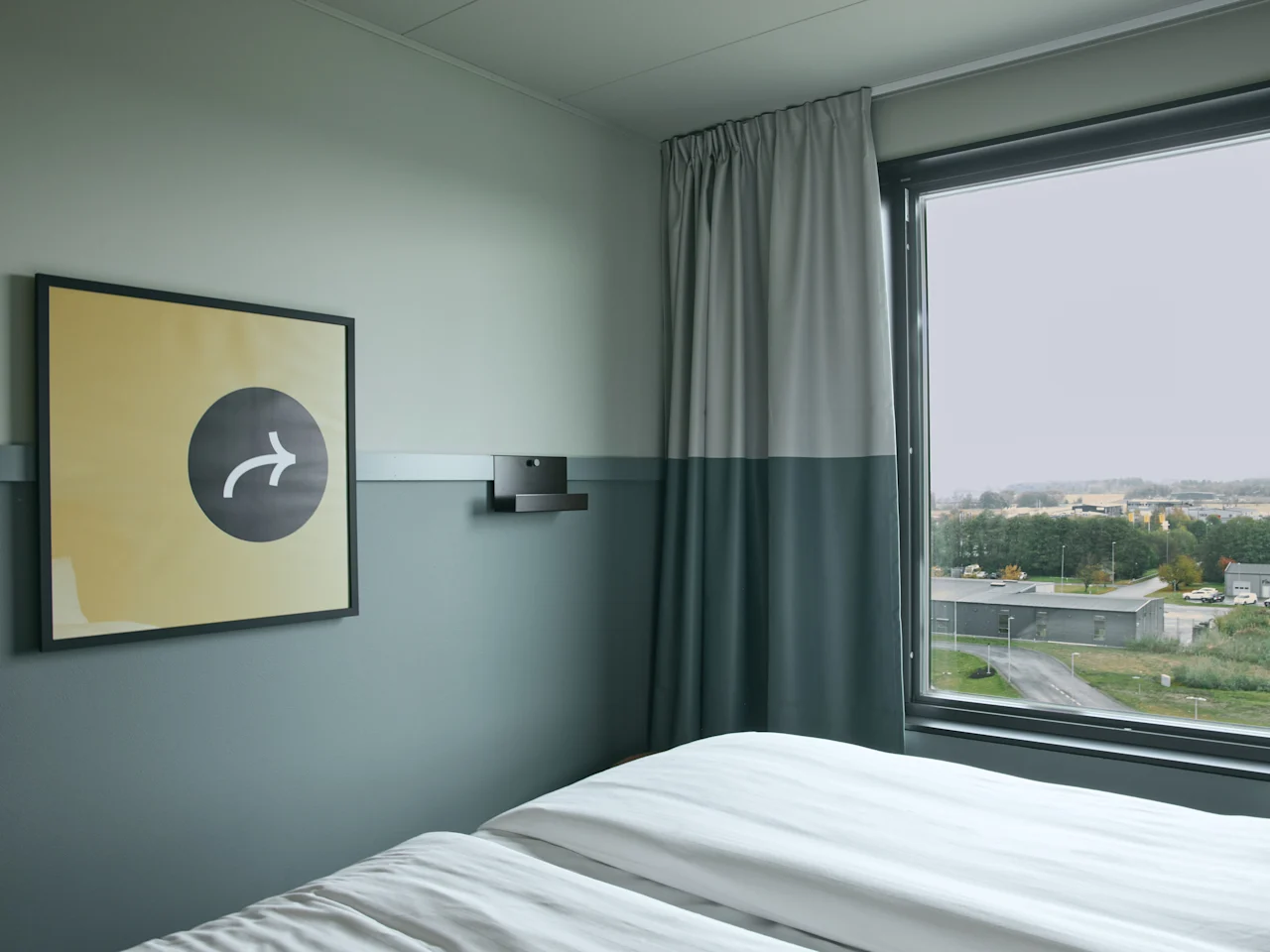 Ett mysigt rum på Stopover Hotel Falkenberg med en bekväm säng, ett fönster med utsikt och en unik väggkonst.