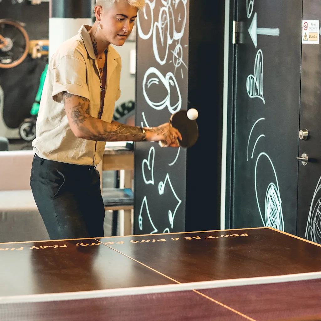 En person spelar bordtennis, håller ett racket och en boll, med texten DONT BE A PING PONG synlig på bordet.