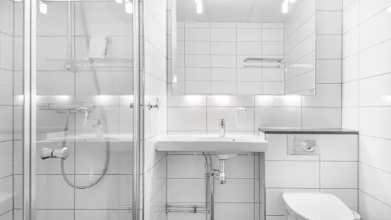 Et lyst, moderne bad med hvite flislagte vegger, med dusj, vask og toalett.