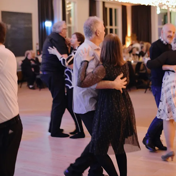 Folk danser i par på et arrangement og nyter musikken og selskapet i en varm, innbydende atmosfære.