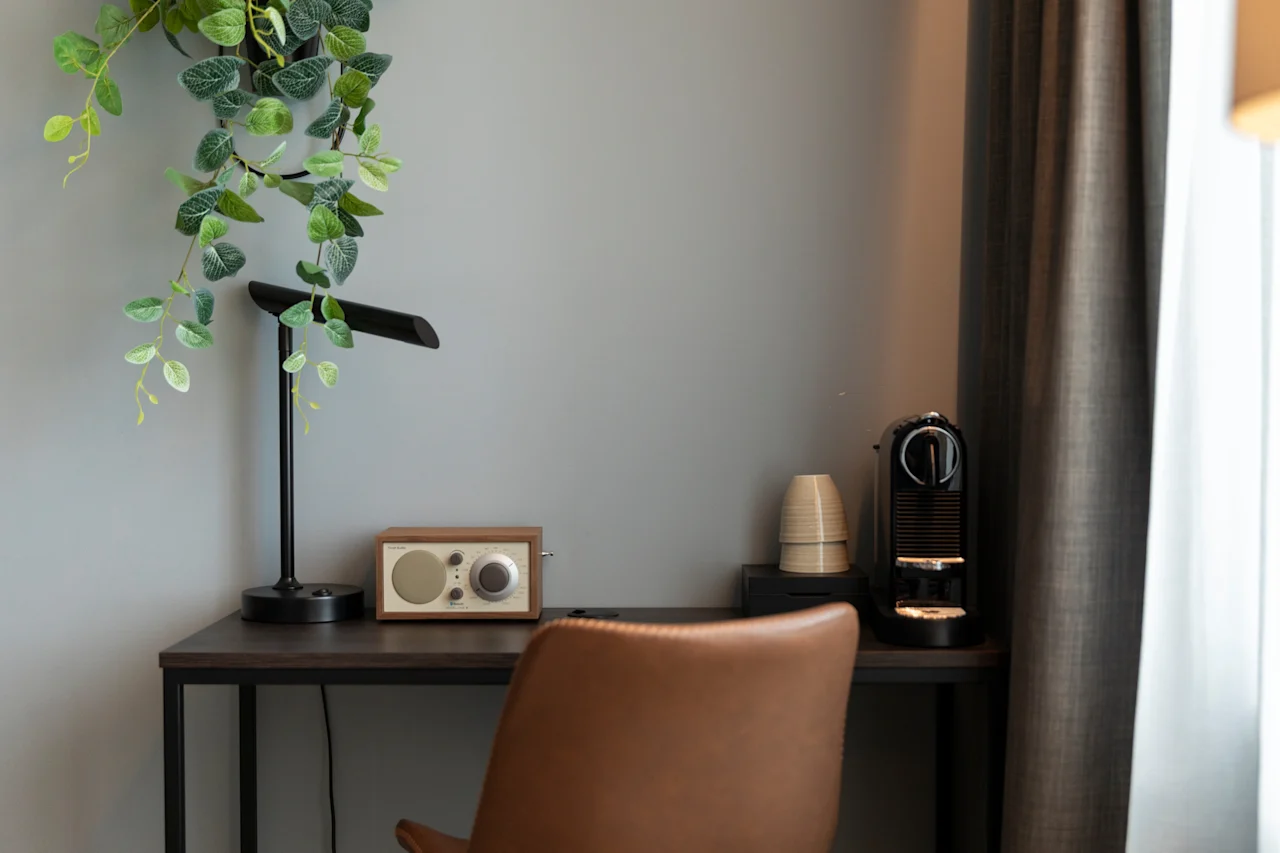 En koselig skrivebordsplass med en plante, en moderne lampe, en radio i vintagestil og en kaffemaskin, ved siden av en komfortabel stol.