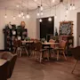 An inviting restaurant or lounge with wooden tables, brown chairs, and exposed light bulbs. A chalkboard sign says THE TASTE OF HOME.