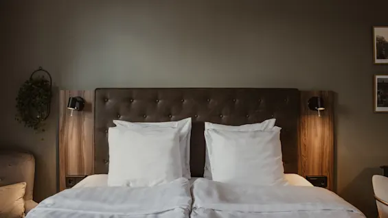 Viihtyisä hotellihuone, jossa on suuri sänky, valkoiset liinavaatteet ja lämmin valaistus, mikä viittaa mukavuuteen ja rentoutumiseen.