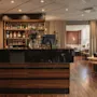Lämmin ja kutsuva hotellibaari ja lounge-alue, jossa on tumma puinen baari, pulloilla täytetyt hyllyt ja mukava sohva.
