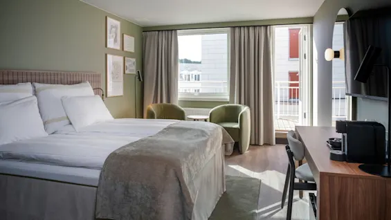 A modern and comfortable hotel room with a bed, a cozy seating area by the window, a desk, and a balcony.