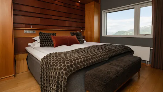 A neatly made bed with decorative pillows in a room with wooden accents and a mountain view through the window.