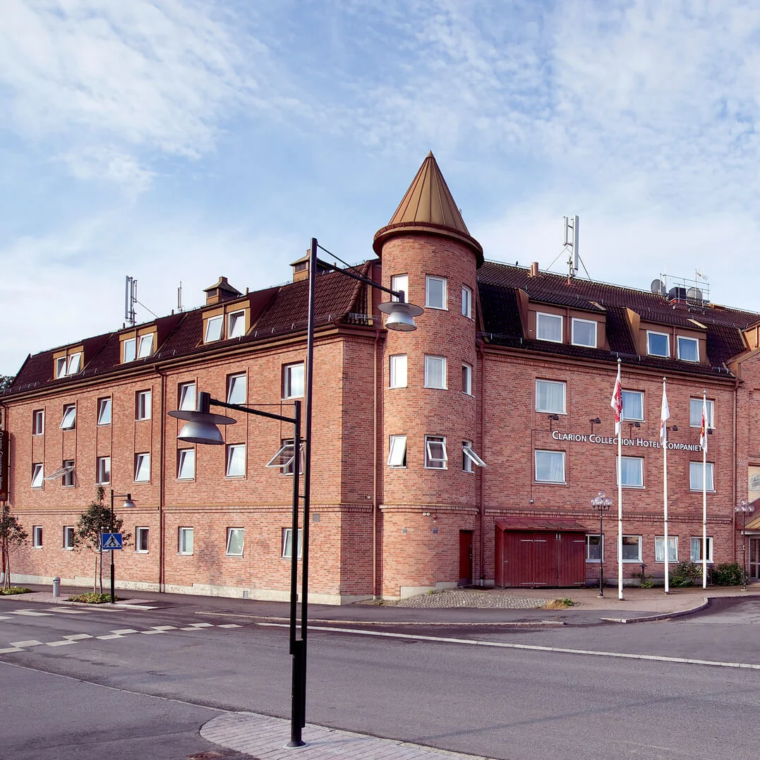 A brick hotel with conical towers stands at a street corner under a partially cloudy sky.