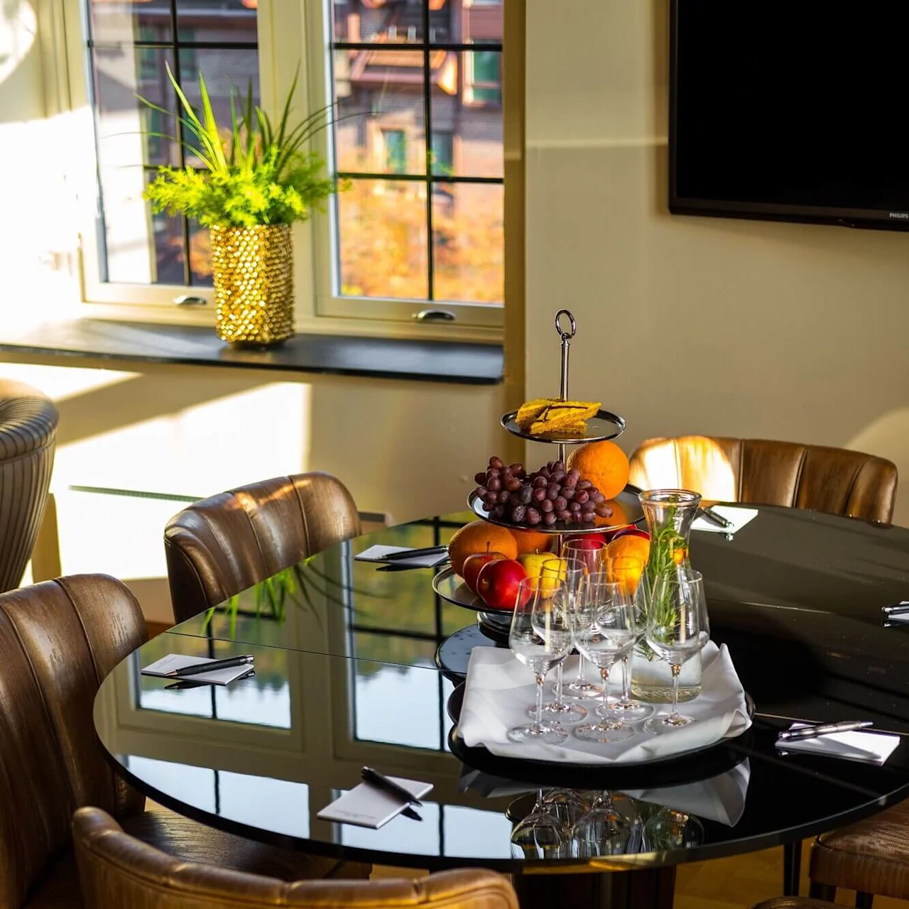 A dining area with a glass table set with fruit and wine glasses illuminated by natural light.