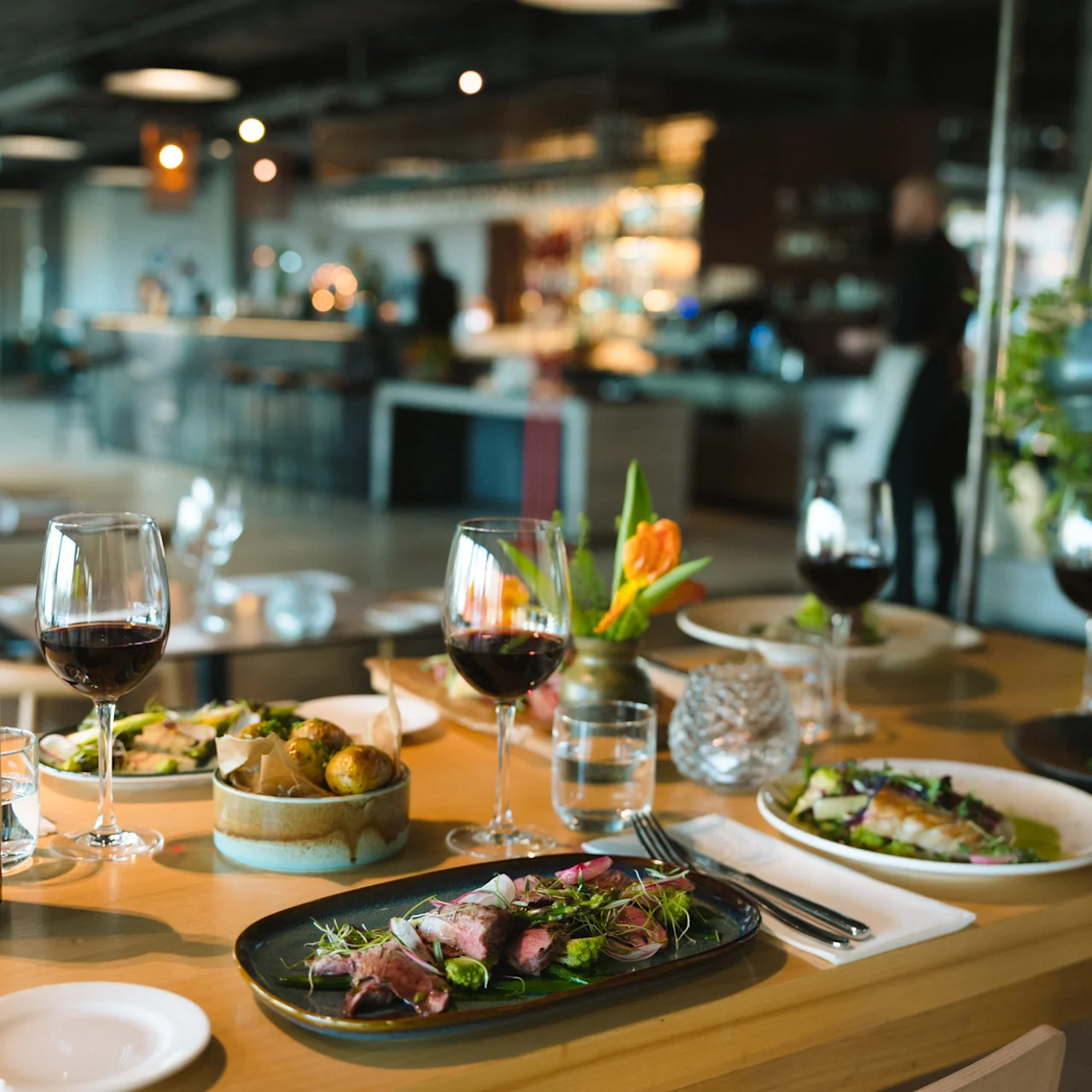 Ett bord med en flaska rött vin, måltidstallrikar och glas; placerat i en stilren, modern restaurang med oskarp bakgrundsaktivitet och mjuk belysning. Text: "414" och "Middle..."