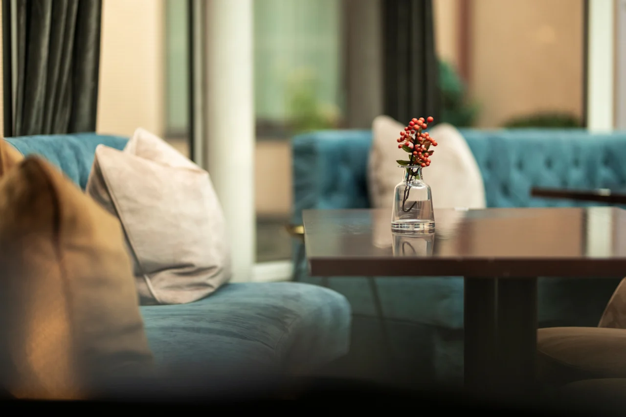 A cozy seating area at Home Hotel Grand Bodø with blue sofas, light cushions, a wooden table, and a vase of red berries.