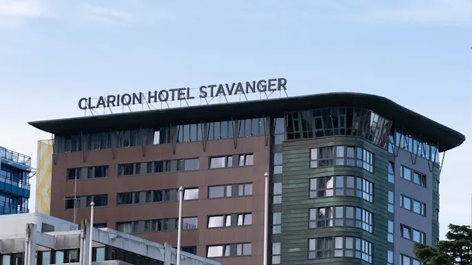Clarion Hotel Stavanger sign sits atop a modern, multi-story building with brown and green panels, surrounded by a clear blue sky.