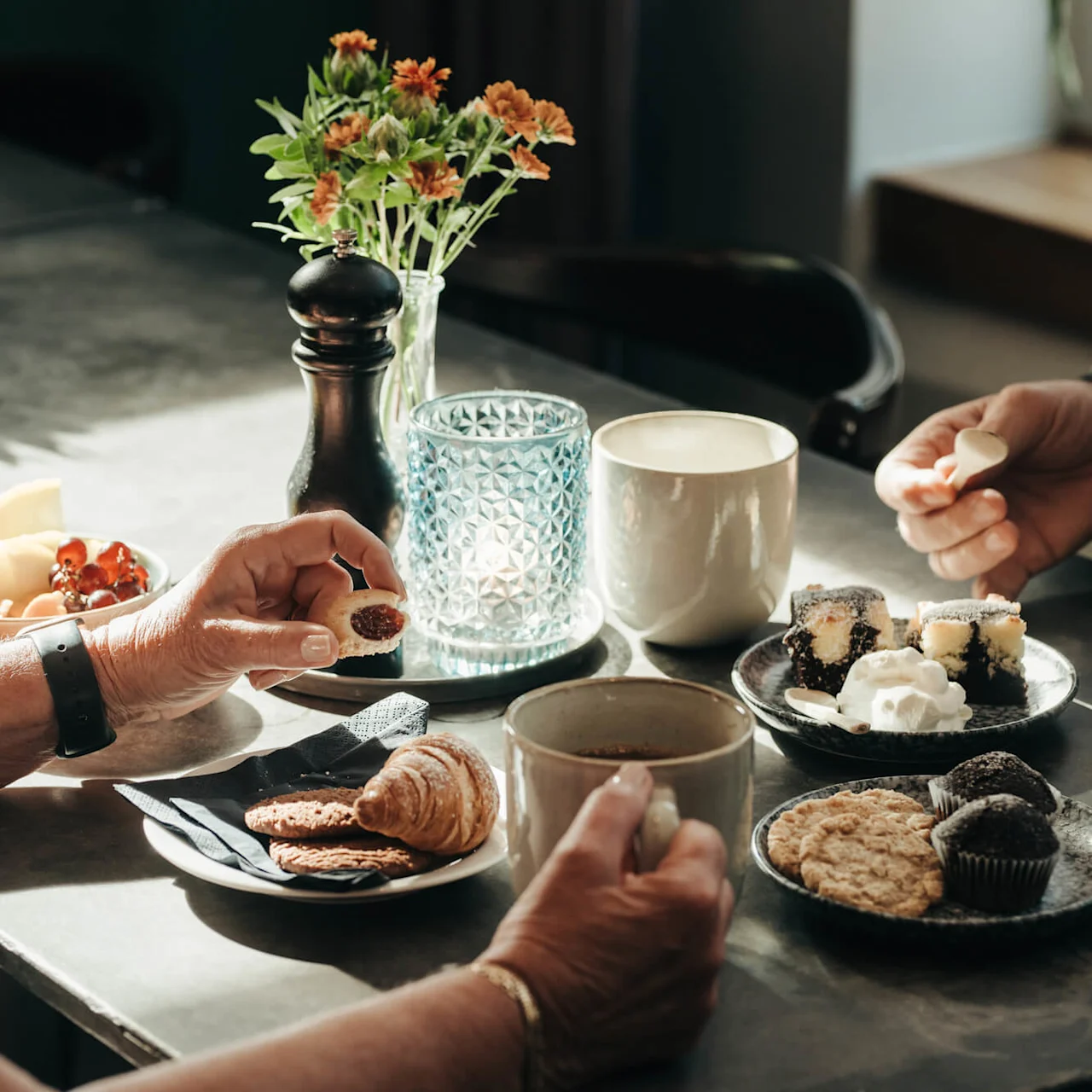 Two people having coffee and pastries at a table with sunlight illuminating the scene.