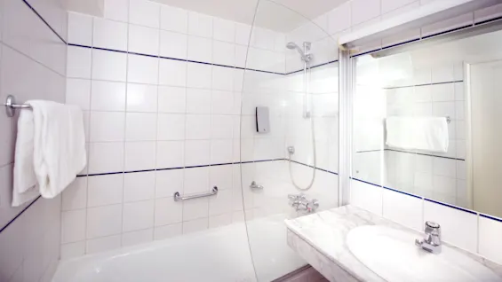 Et rent badeværelse med hvidt badekar og håndvask, reflekteres i et spejl; håndklæde på stang, moderne fittings.