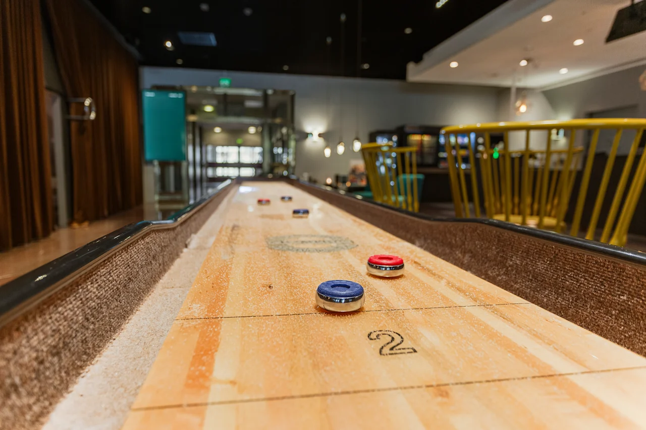 A shuffleboard game with red and blue pucks and the number 2 on the table, set in a modern and inviting lounge.