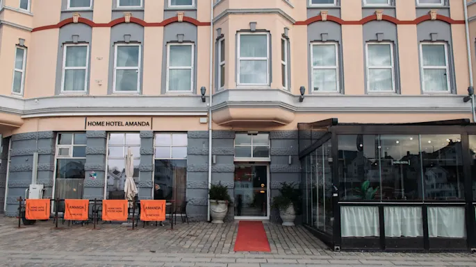 En sjarmerende bygning med skiltet HOME HOTEL. Rød løper til inngangen, med uteservering og et innglasset område.