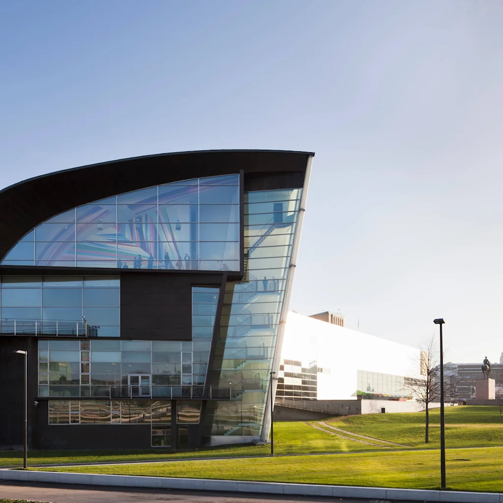 Museum of Contemporary Art Kiasma, en modern byggnad med böjt tak och stora glasfönster, omgiven av grönt gräs.