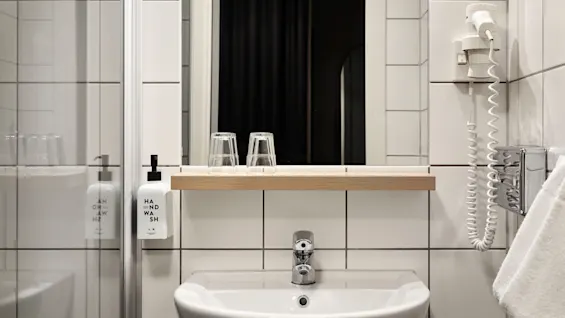 Ett rent hotellbadrum med handfat, spegel, handtvål och hårtork, redo att användas.