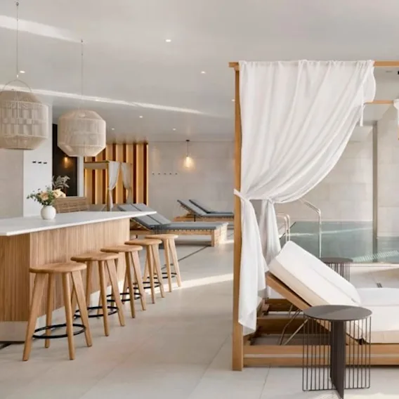 A tranquil spa interior with lounge chairs, sheer curtains, and a pool, featuring a warm, minimalist design and soft lighting.
