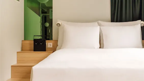 A modern bedroom at hobo oslo with a comfortable bed, wooden steps, and green accents.