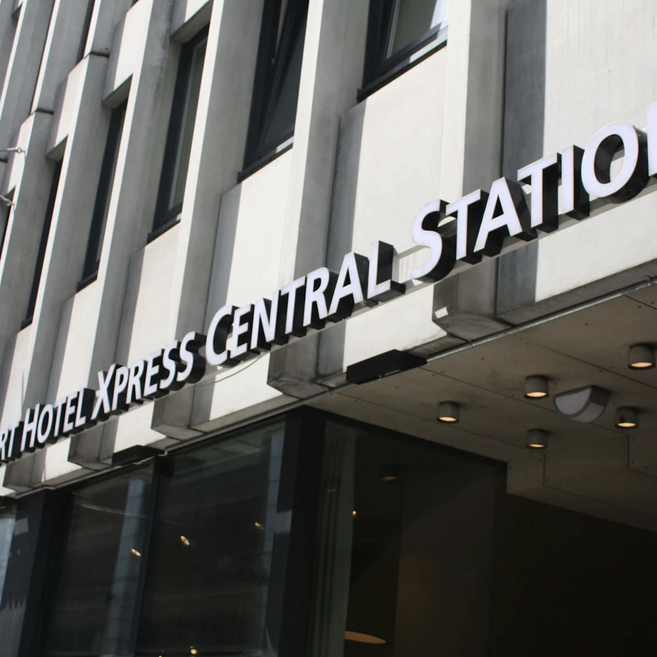 The sign reads "COMFORT HOTEL XPRESS CENTRAL STATION" in large letters on a modern building facade with windows, under a sunny sky.
