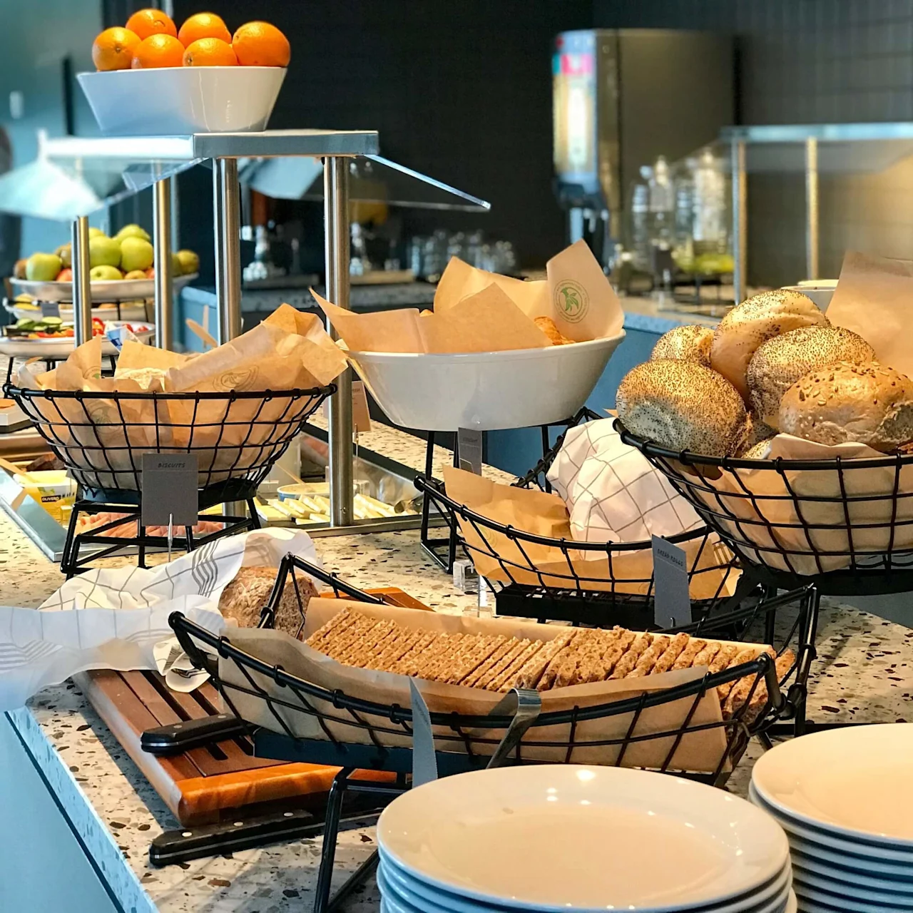 Skåle og kurve viser forskellige brød på en marmor buffet, omgivet af appelsiner og andre frugter i et moderne, godt oplyst spiseområde.