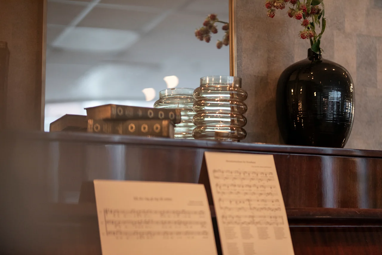 A piano with sheet music, decorated with books and vases, at Home Hotel Grand Bodø.