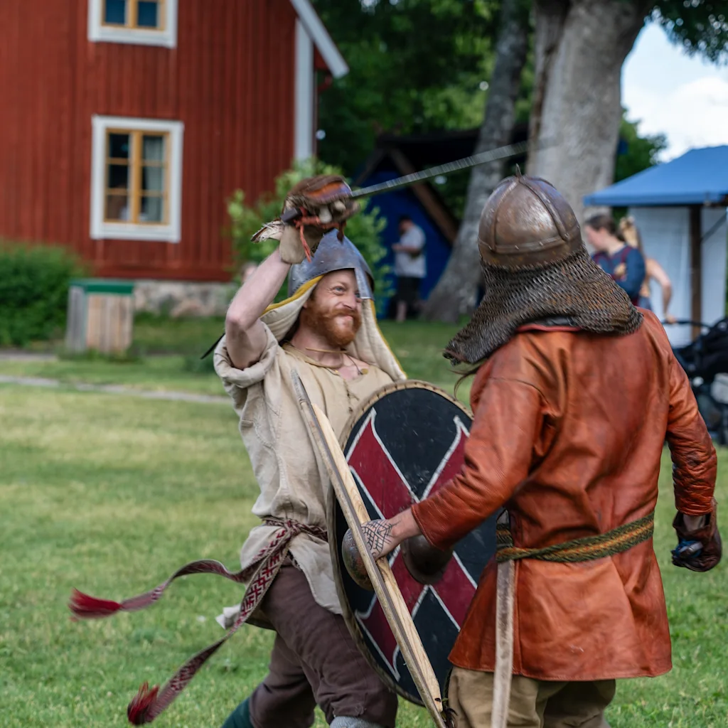 En livlig historisk återskapelse i Uppsala, som visar två deltagare i en svärd- och sköldstrid.